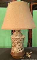 Front view of the pottery lamp with textured ceramic base and beige fabric lampshade on top.