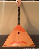 Front view of a triangular wooden string instrument with one string broken, showing front painted decorations and fretboard