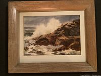 Framed watercolour painting showing waves crashing on rocks with foam and spray. Wood frame and mat visible.