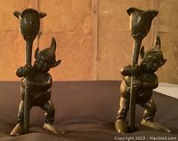 Front view of the pair of brass elf candlestick holders, showing detailed elf figures holding tulip-shaped candle cups.