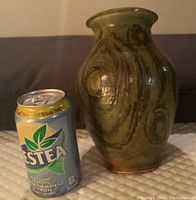 Hand turned pottery vase beside a soda can for scale, showing shape, glaze, and pattern details.