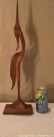 Side view of tall teak wood bird carving next to a can for scale showing detailed profile and base dimensions.