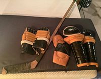 Photo showing vintage Boston Bruins hockey gear laid out on a black surface, including gloves, shin pads, elbow pads, and hockey stick.