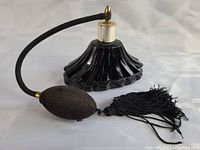 Full view of vintage black glass perfume atomizer with bulb and tassel lying on its side