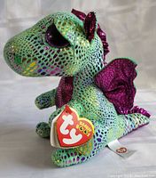 Front and side views of Cinder Beanie Boo TY dragon plush, showing shiny scales, purple wings, and original TY tag.