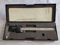 Overall view of the electronic digital display caliper inside its black plastic carrying case with foam insert and instruction sheet.