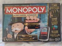Front of unopened Monopoly Ultimate Banking board game box showing Mr. Monopoly holding a credit card and the electronic banking unit.