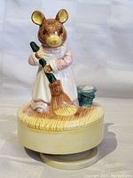Front and side view of detailed ceramic mouse music box holding broom and standing next to a small bucket on round base.