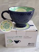 Photo showing the textured dark blue porcelain mug with handle, tag attached, and box indicating it is a Native Home Moon design porcelain art mug with 12 oz capacity.