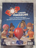 Front view of the Pop Under Pressure game box showing game title and artwork of cartoon players around a balloon.