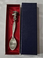 Photo of pewter Snoopy spoon in red-lined box with dark blue textured cover.