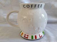 Side view of white ceramic Starbucks coffee mug shaped like a globe. Embossed continents visible. Base decorated with flags including Norway, Italy and Switzerland. Rim shows black text 'COFFEE'.