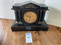 Front view of black antique Ansonia mantel clock with ornate gold face and two columns on each side.