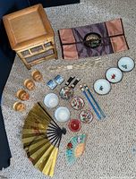 Wide shot of multiple Asian decor items arranged on carpet showing wooden stand, lacquerware, ceramic bowls, chopstick rests, decorative fans, chopsticks, and fabric item