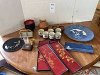Overview of the lot showing all plates, bowls, tea cups, nut dish, four red lacquer panels, and compact on a wooden table.