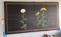 Full view of the four-panel screen hanging on wall showing chrysanthemum designs in white, yellow, and green on dark background with gold accents.