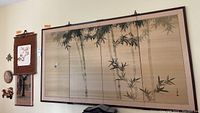 Full view of wall with hanging Asian decor including large painted fabric four-panel screen and smaller wall arts.