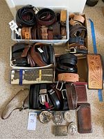 Overhead view of multiple bins containing assorted leather belts, buckles and wallets on carpet