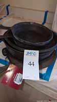 Stacked cast iron pans showing frying pans on top, griddle and pie plate beneath. Visible tag on one pan.