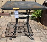 Front angle view of iron patio table showing mesh top, umbrella hole and base structure with rust spots.