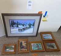 Overview photo showing large pastel of dog sled scene and four smaller framed pastel wildlife artworks on carpeted floor