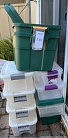 Stacked storage bins in various sizes, primarily green and clear with lids. Labels and tags visible.