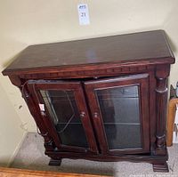 Front angled view showing dark wood finish, glass doors, and decorative front columns