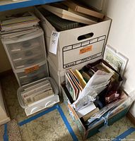 Boxes and plastic storage drawers filled with assorted stationery papers, greeting cards, envelopes, and postcards