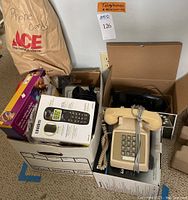 Lot of multiple telephone sets and accessories packed in boxes including beige Princess style phone and black rotary phone.