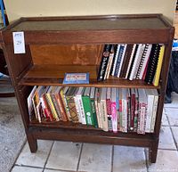 Front view of vintage wood bookcase with two shelves filled with assorted cookbooks and bookends