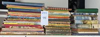 Wide photo showing several dozen stacked children's books including classic titles like The Wizard of Oz, arranged in rows on a shelf.