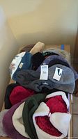 Top view of the collection of knit, faux fur, and fleece men's hats piled in a box, showing different colors and styles.
