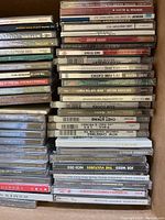 Cardboard box packed with stacked music CDs in jewel cases showing titles like Motown Legends and Best of Funk Classics