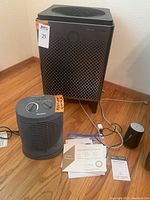 Three appliances (air purifier, space heater, humidifier) with manuals and power cords on hardwood floor