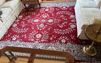 Full view of large wine red area rug with floral and vine patterns, blue/gray border and off-white fringe between furniture.