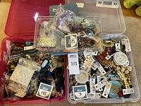 Three clear plastic storage boxes filled with a variety of beads, including loose and bagged beads of multiple colors and styles.