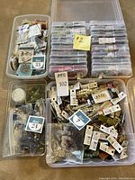 Three open-top bins and stacks of small compartment boxes filled with assorted packaged bead strands and loose beads