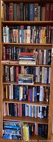 Tall wooden bookshelf filled with assorted books of varying colors and sizes, some stacked horizontally