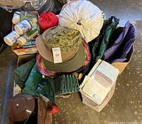 Photo showing assorted camping gear including sleeping bag, hats, camp chairs, stuff sacks, and other gear stacked together.