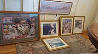 Overview of all framed art prints including Jeanniot, Monet, Rockwell, and Golden Gate prints displayed on carpet and against wall.