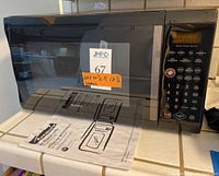 Front view of Kenmore microwave with control panel and manual underneath.