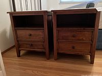 Front view of the pair of medium dark wood bedside tables showing the two small drawers and cubby space on each.