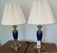 Front view of both brass and blue Stiffel table lamps with pleated white shades.