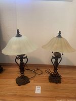Pair of metal frame table lamps with frosted glass shades and pull chain lights, sitting on wooden floor.