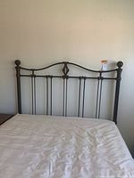 Front view of queen metal bed frame headboard with decorative metal design and rounded finial bedposts.