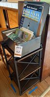 Small shelf unit holding a metal container filled with assorted folded maps and a blue AAA North American Road Atlas.