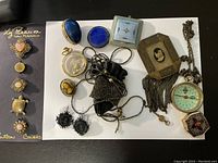 Small Victorian style collectibles on white background including brooch, button covers, enameled boxes, earrings, compass, pouch.