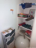 Shelves containing dumbbells, ankle weights, tennis racket, exercise ball, fishing pole and boxes.