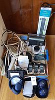 Various vintage and newer electronics including headphones, power strips, cordless phones, and radios arranged on a wooden floor.