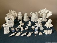 A wide view of the 23 white ceramic pieces spread out on a table, including various animal and character figurines, decorative items, and two jars of sparkle color wash.